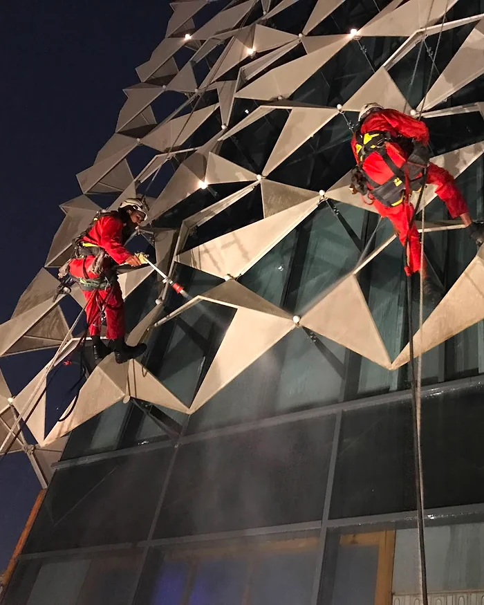 فنيان على حبال يغسلان واجهة معدنية مضلعة ليلاً بماء مضغوط